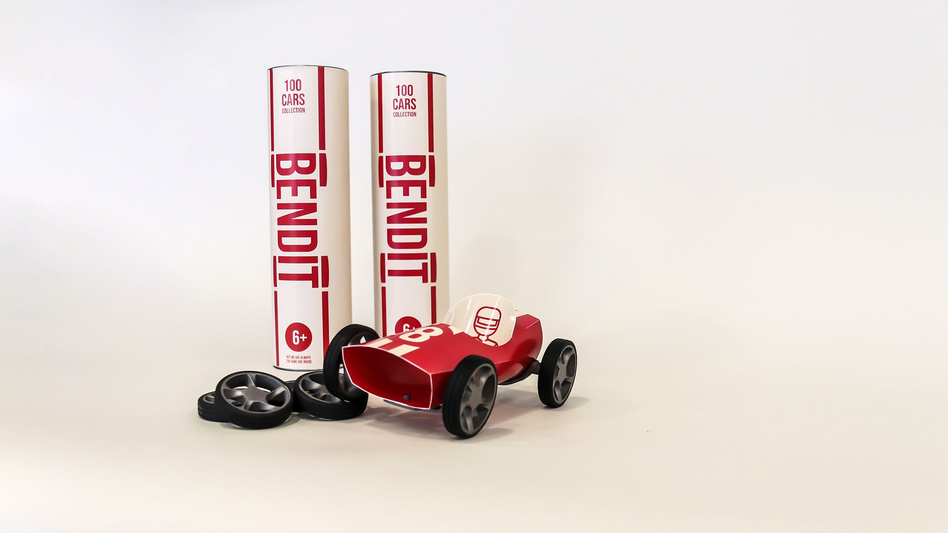 A red Bendit car beside two cylindrical BENDIT packaging tubes marked 6+.