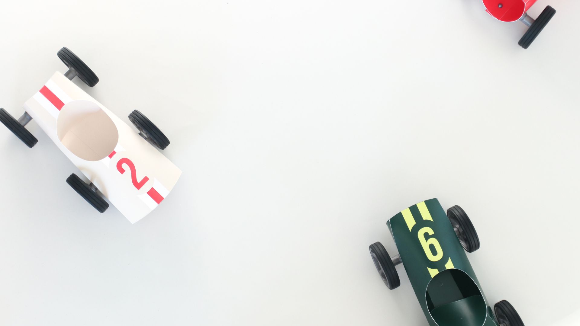 A white number-2 Bendit car and a dark-green number-6 car on a white surface.